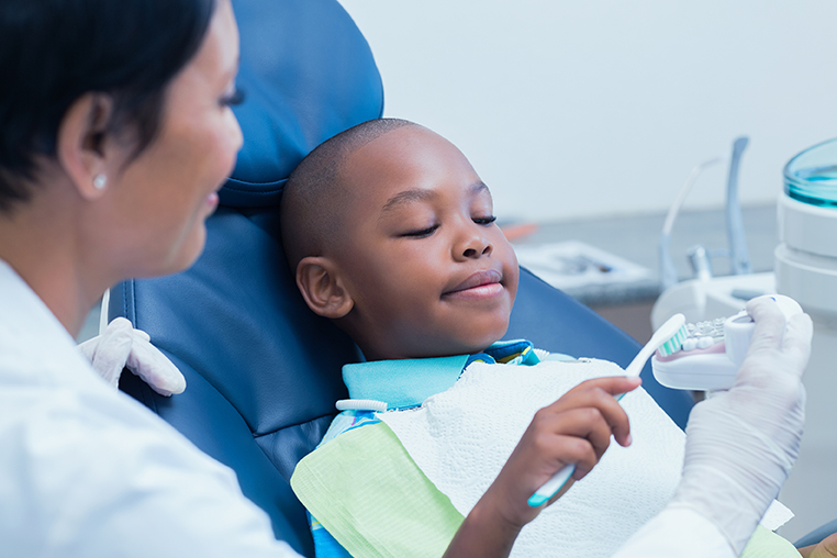 Dental healthcare provider showing boy how to brush teeth.