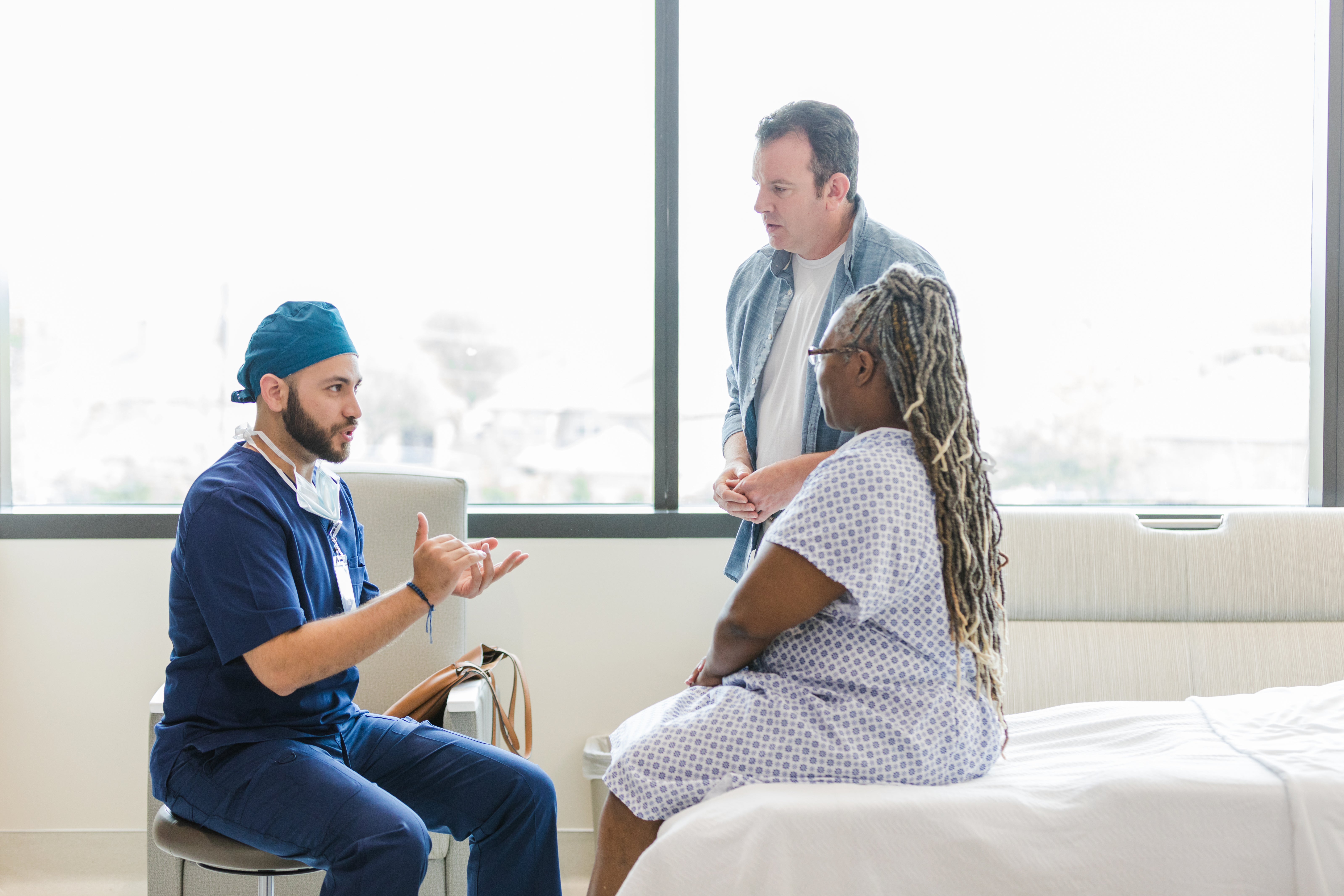 A health care provider talks to a woman wearing a hospital gown and her partner