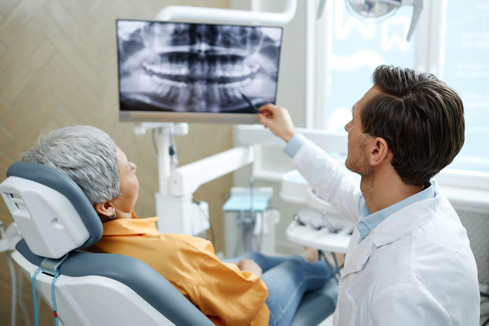 Back view of male dentist pointing at tooth X-ray image on screen