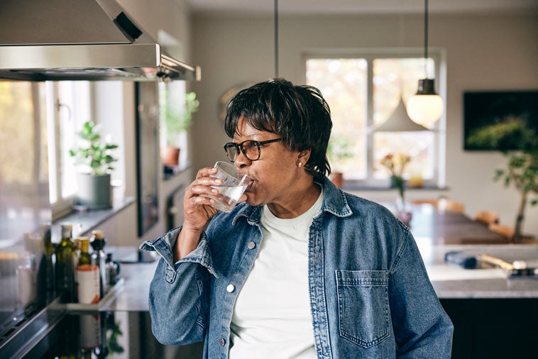 Older woman drinking glass of water in kitchen