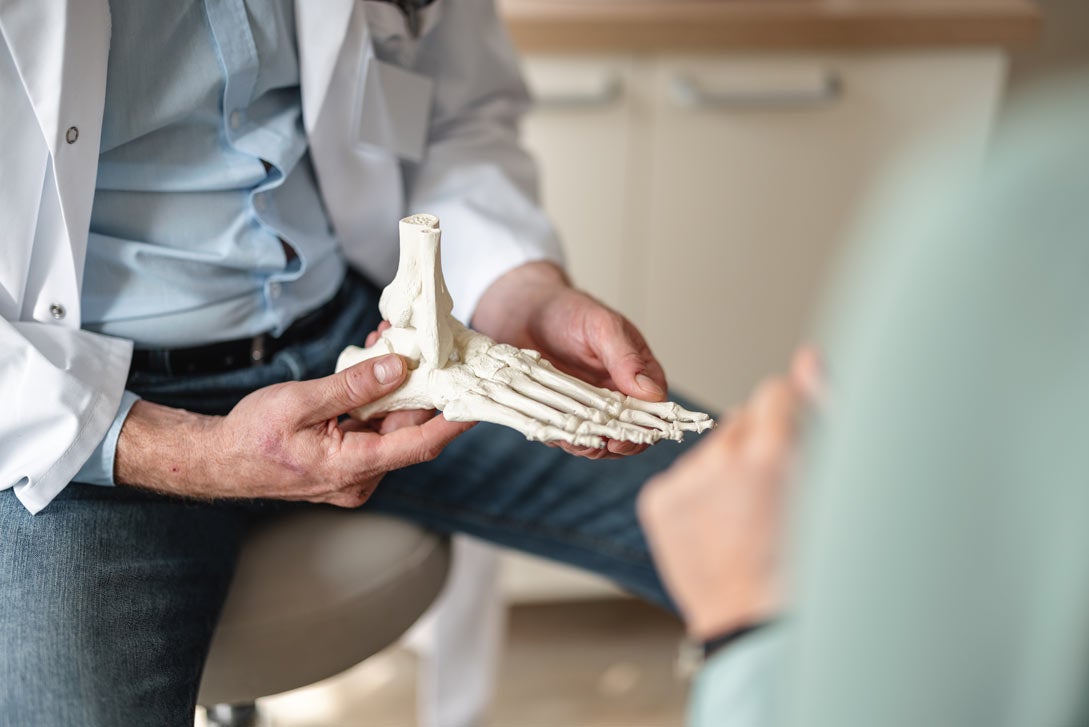A doctor uses a model foot to show a patient how rheumatoid arthritis affects the joints