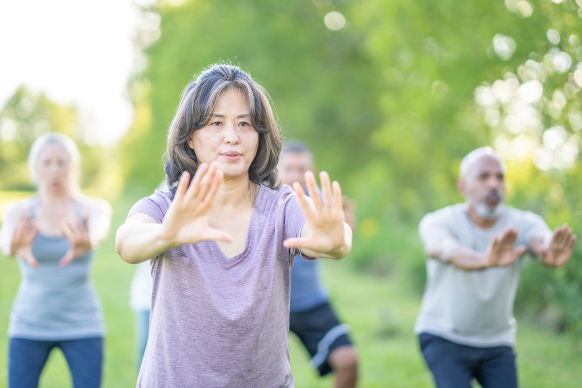 group of older people does tai chi outside, close up on female leader