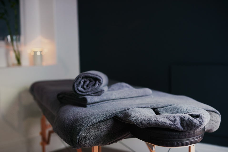 A wooden massage table with gray bedding and towels