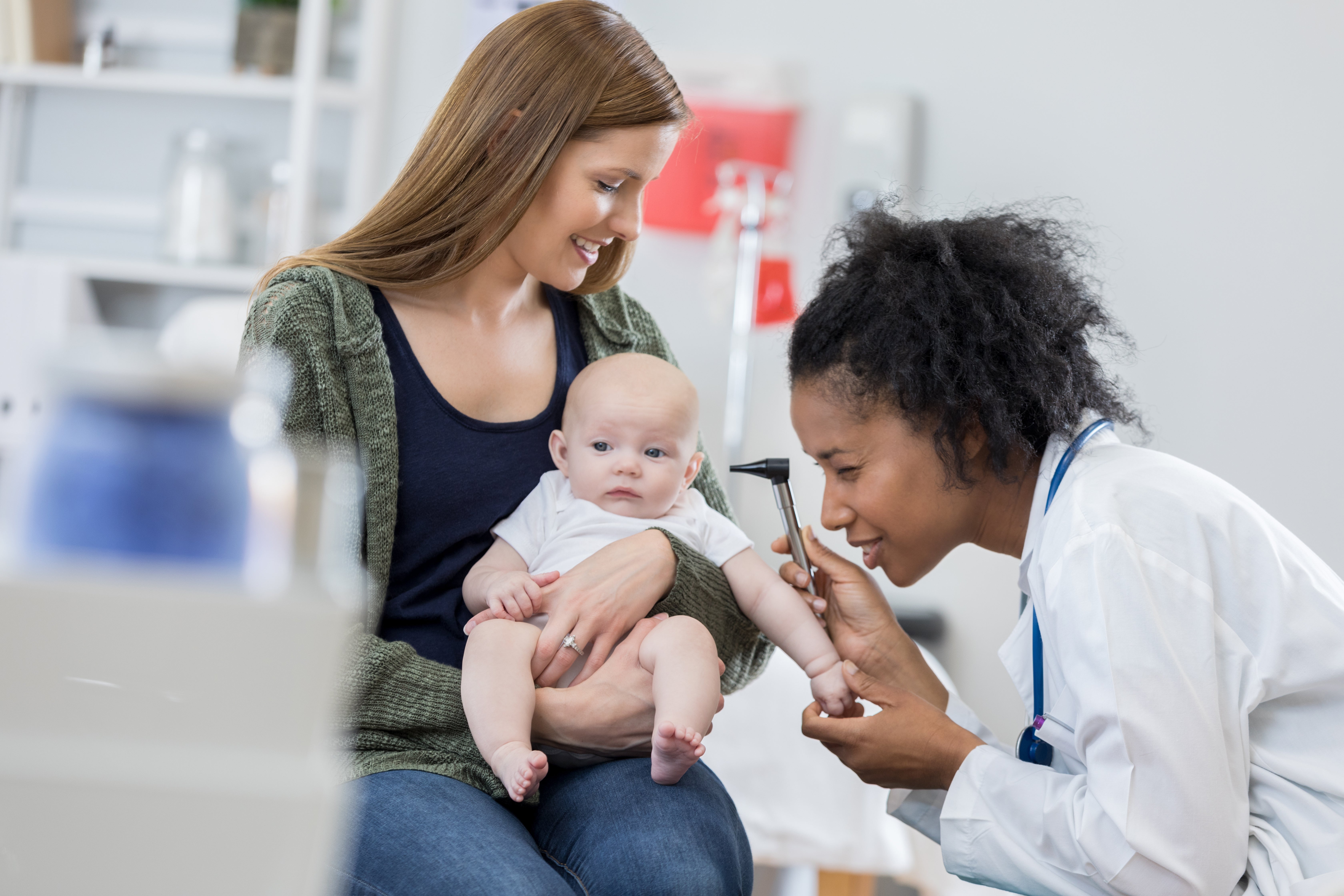 A mother holds her baby as a doctor examines the baby's ear