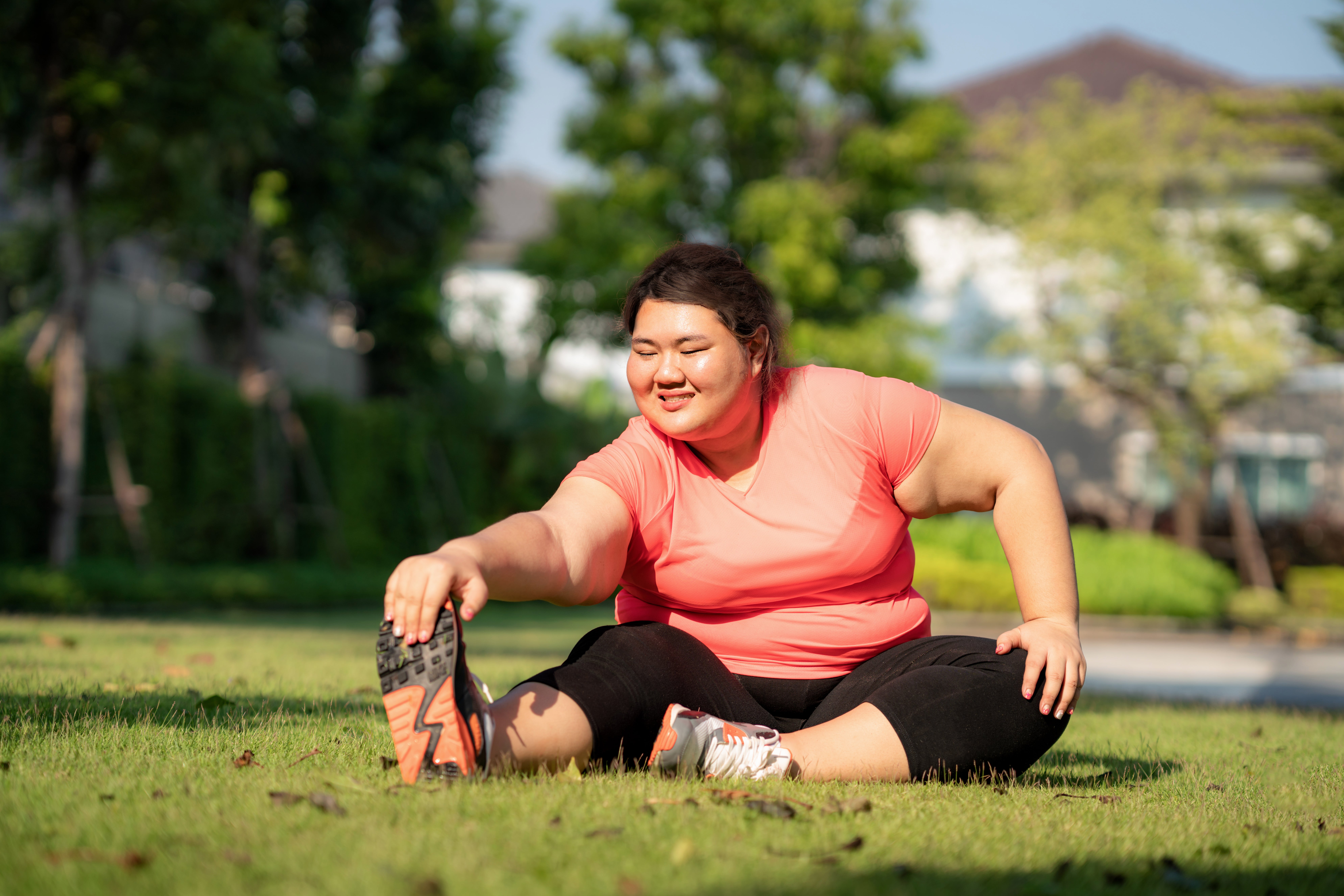 A plus size woman stretches while exercising outdoors