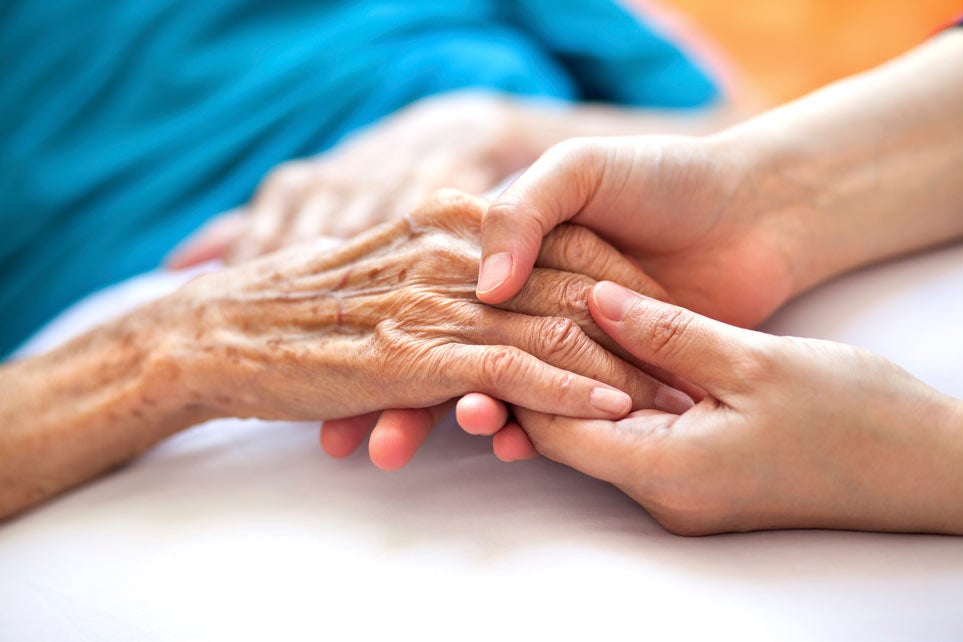 Woman holding senior woman's hand on bed.
