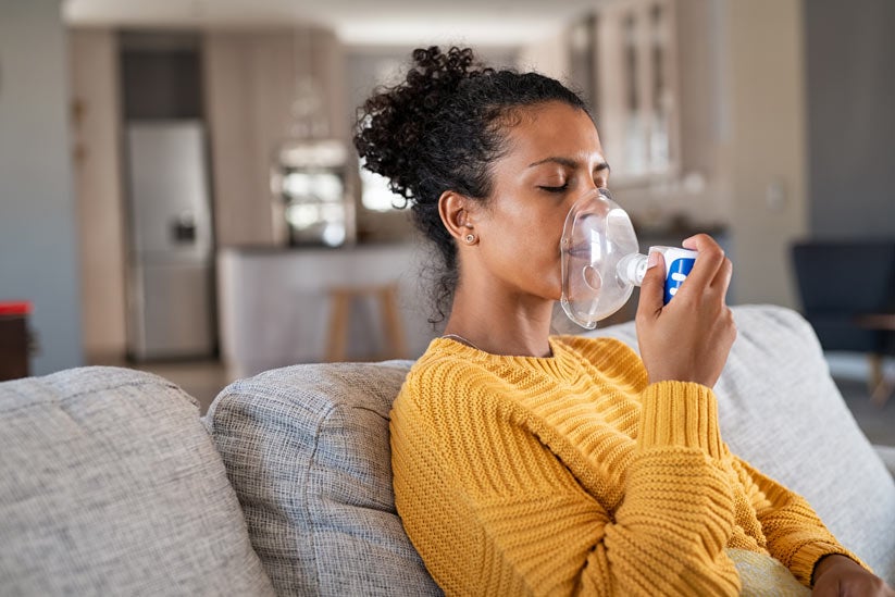 African american woman using nebulizer inhaler at home