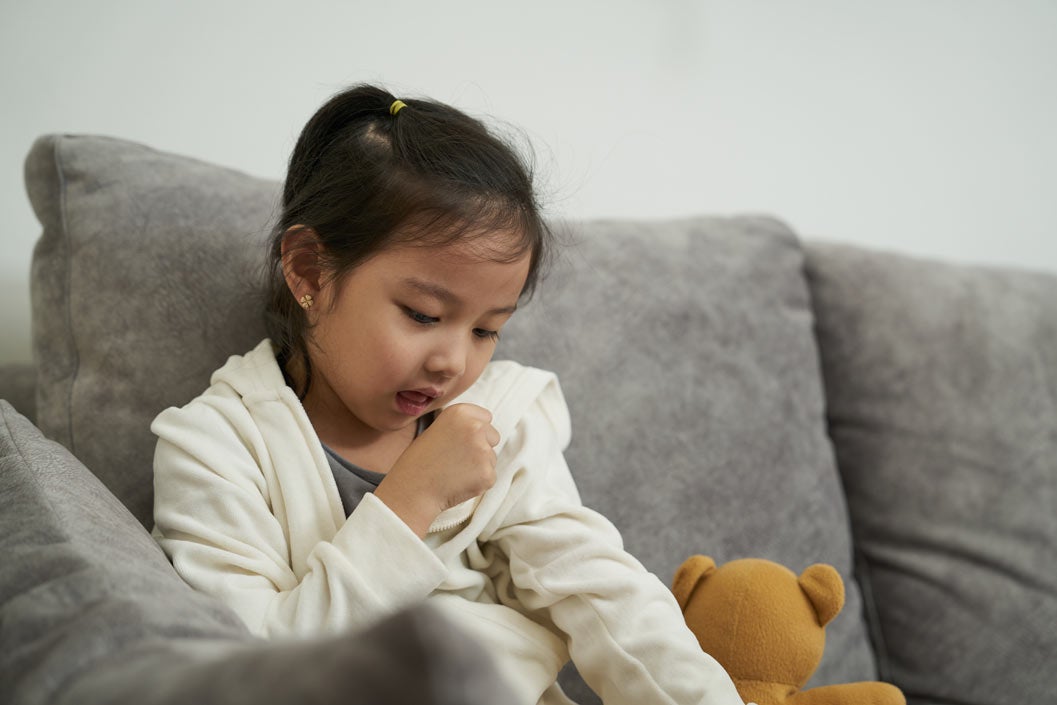 Child sitting on couch coughing into her hand