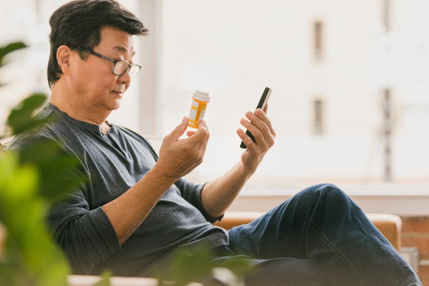 Older man with glasses holding up pill bottle and phone