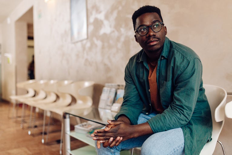 Man in green shirt sitting in waiting room outside of medical clinic