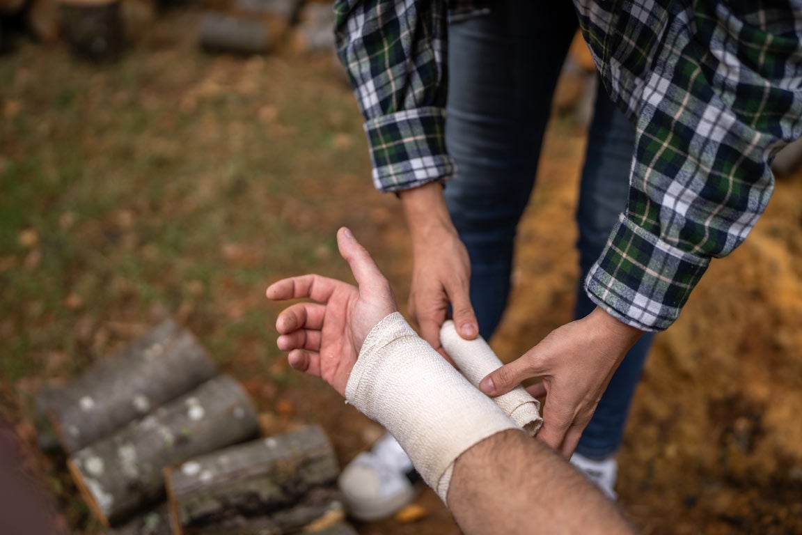 Woman in flannel bandages man's wrist while camping outdoors